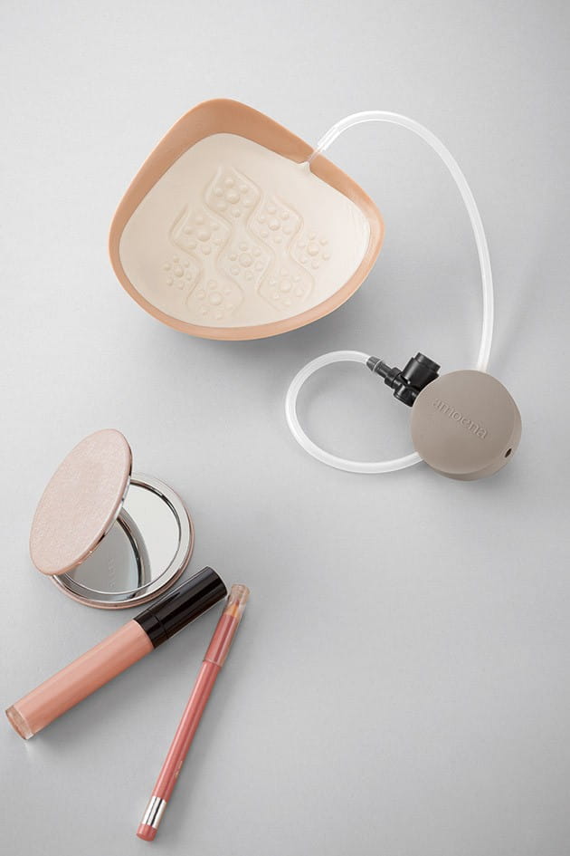 Eine Adapt Air Brustprothese mit angeschlossener Pumpe, die auf einem grauen Untergrund liegt