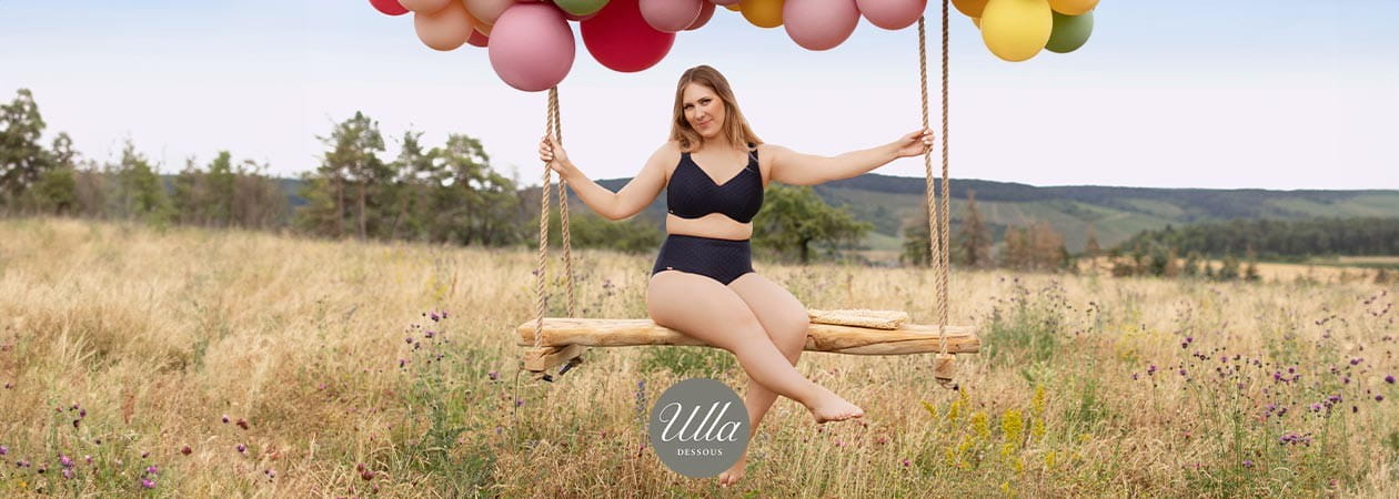 Eine junge, mollige Frau sitzt in einem Wildblumenfeld auf einer Schaukel und trägt Bikini Monaco von Ulla