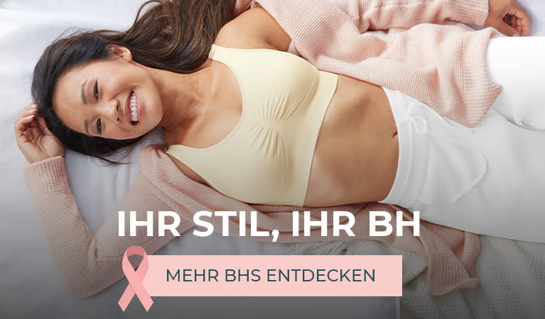 Eine fröhliche junge Frau, die mit einem Prothesen-Bustier von Amoena in einem weichen Bett liegt