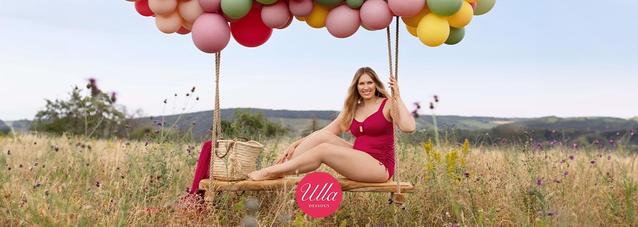 Eine junge, mollige Frau sitzt in einem Wildblumenfeld auf einer Schaukel und trägt Tankini St. Tropez von Ulla